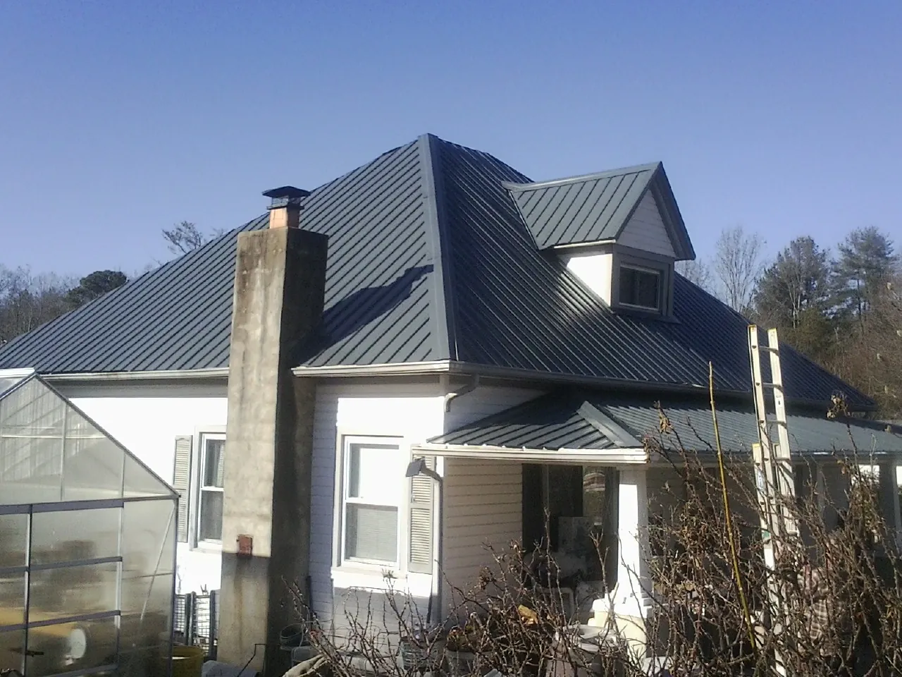Dark blue standing seam metal roof on a white farmhouse with dormer — Slate & Tile Roof Repair by Roofing Brothers in Evans Mills