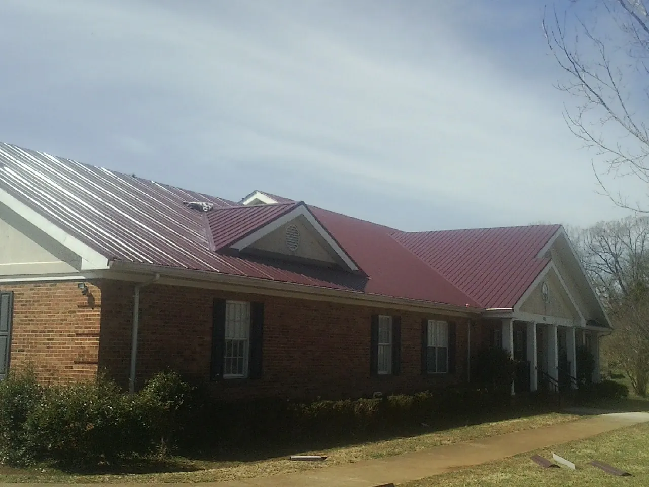 Red metal roof with gabled entries on a long brick building, from a Hail Damage Roof Repair job in Evans Mills