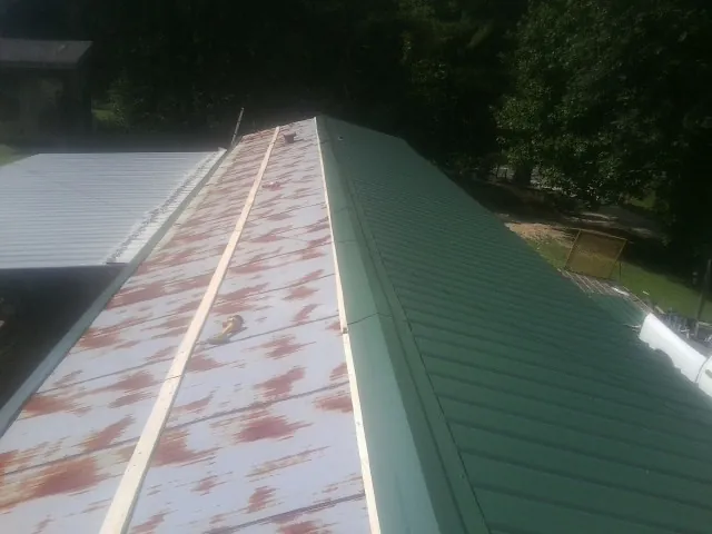 Old rusted panels beside newly installed green metal roofing — Wind Damage Roof Repair by Roofing Brothers in Evans Mills