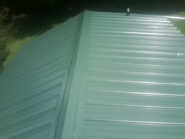 New green metal panels meeting at the ridge of a roof — Flat Roof Repair work by our crew in Evans Mills