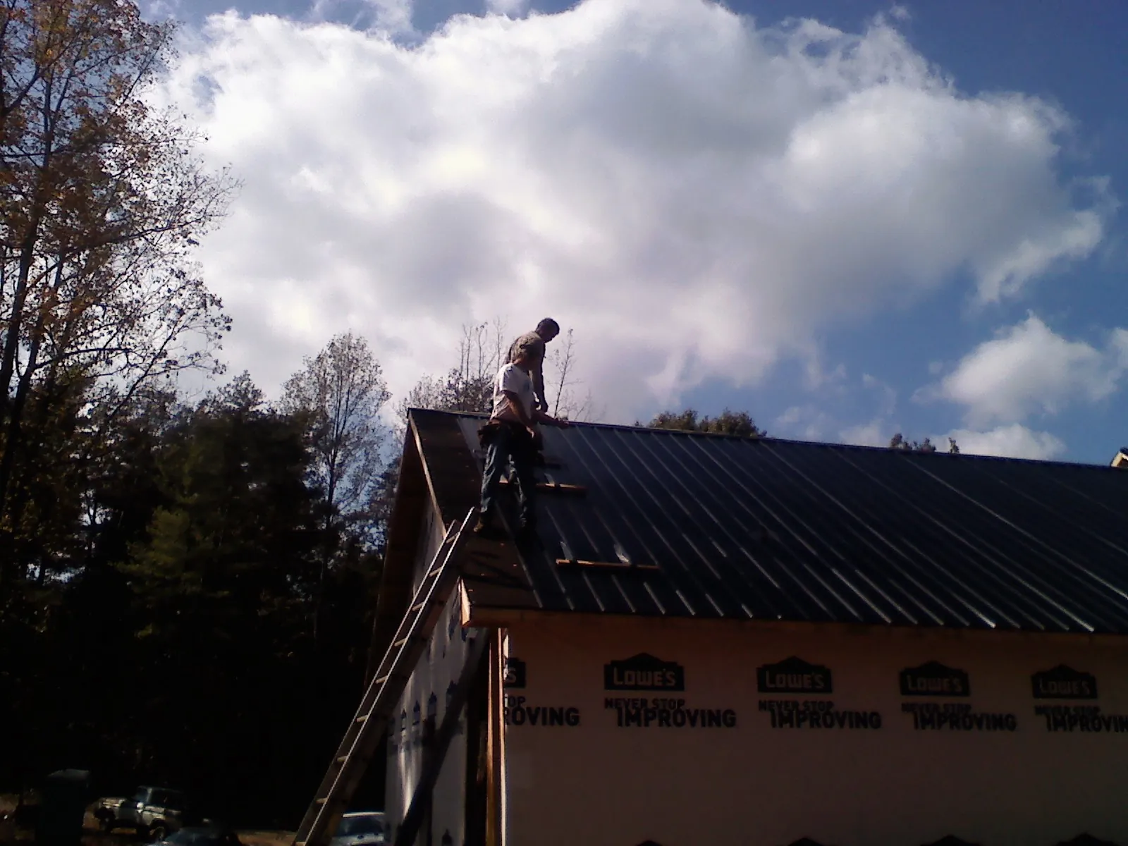 Roofer fastening dark metal panels high against a cloudy sky, from a Roof Inspection job in Evans Mills