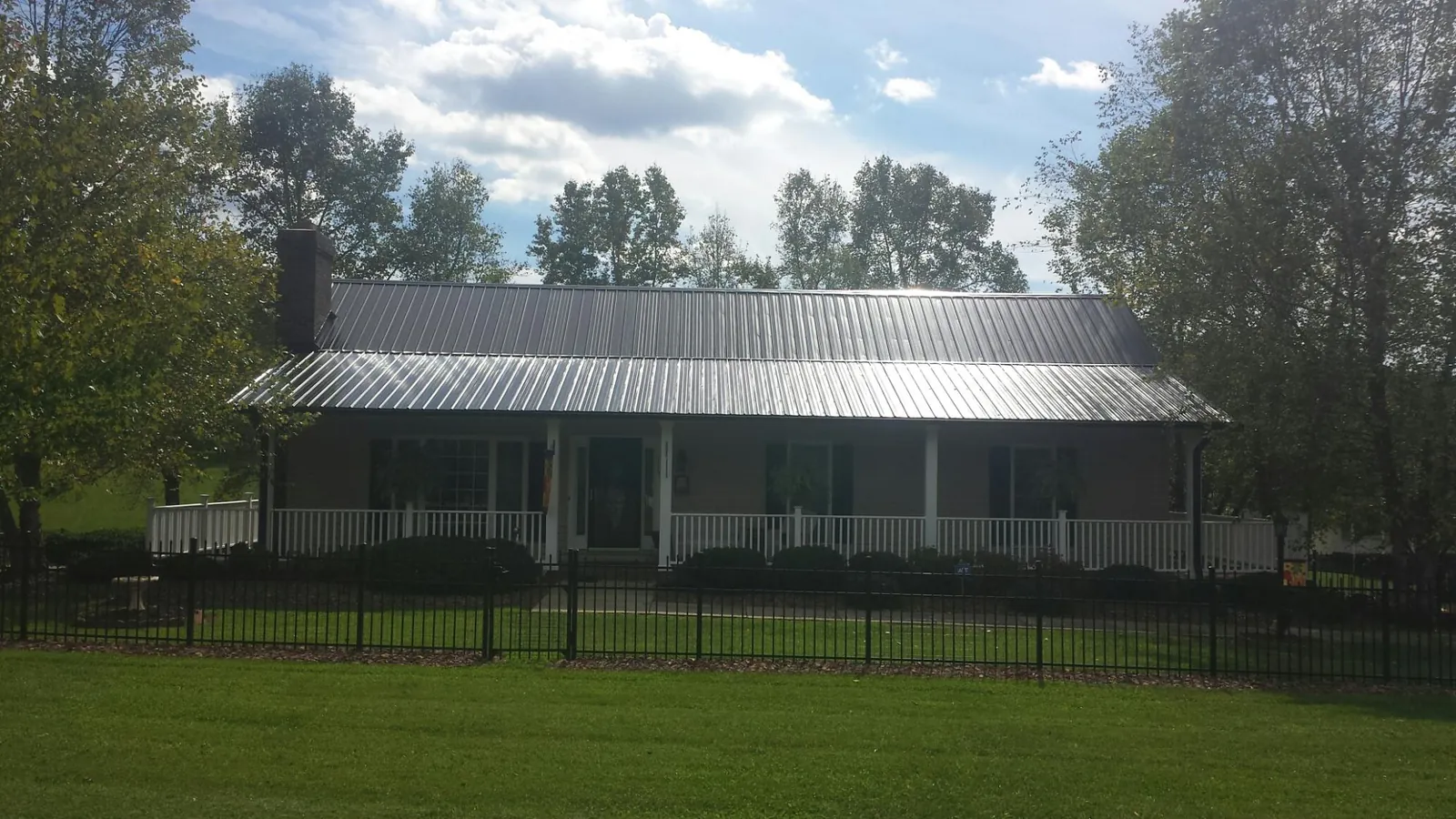 Gray metal roof on a brick ranch with a full width front porch — Gutter Guard Installation work by our crew in Evans Mills