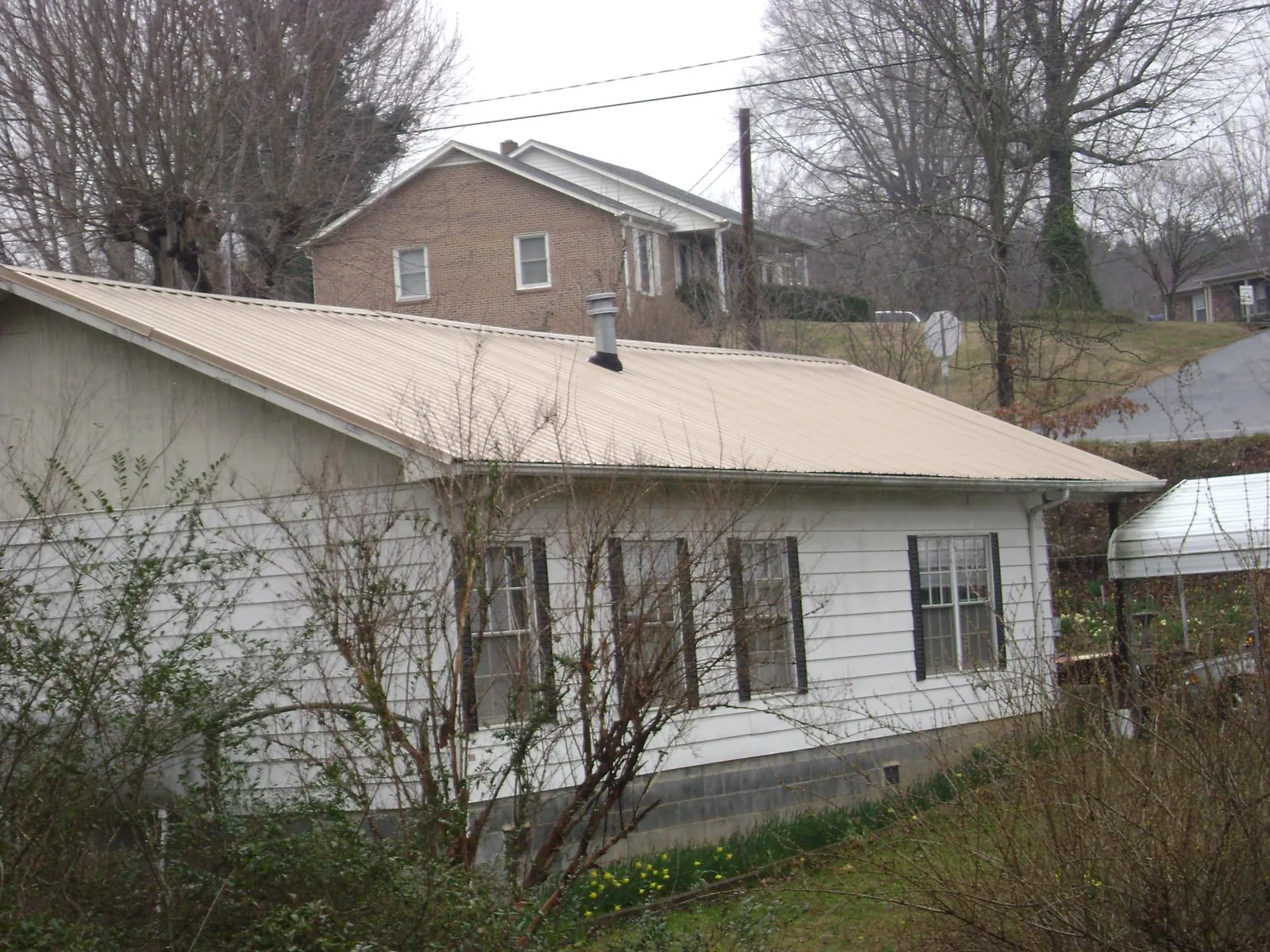 Tan metal roof on a white sided house set into a hillside — Commercial Roofing by Roofing Brothers in Evans Mills