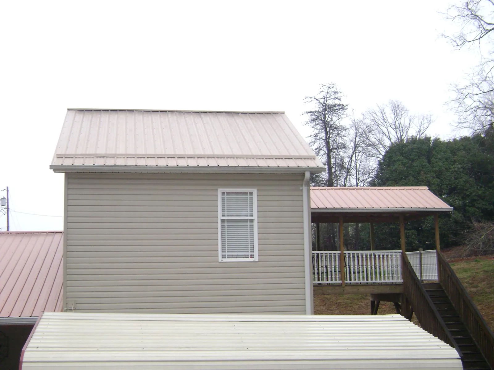 Tan metal roofs on a two story addition and attached porch, from a Roof Replacement job in Evans Mills