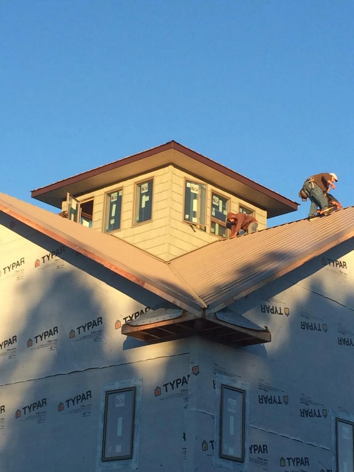 Roofers working around a rooftop cupola on a new metal roof at sunset — Roof Waterproofing in Evans Mills by Roofing Brothers